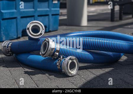 A coiled blue industrial suction hose (siphon pipe) with metal couplings lies on a concrete surface. Stock Photo