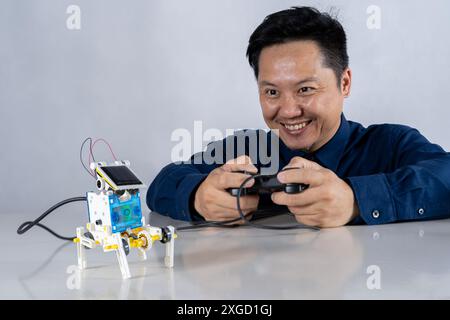 Asian man is building a robot project in his home. Robots control science lessons and coding, developing learning innovations Close-up view Stock Photo