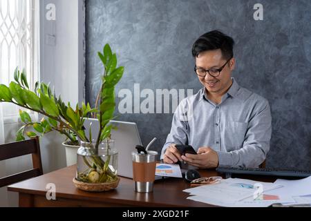 Confident smiling businessman using smartphone in a home office. Checking new e-mails. Businessman holding smartphone sit in office working online on Stock Photo