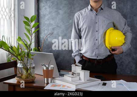 Engineer holding helmet checking accuracy of building structural blueprints from architect on the desk in office to proceed with the construction, eng Stock Photo