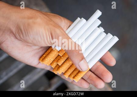 A close-up of a hand holding multiple cigarettes with white filters and orange-brown paper. Stock Photo