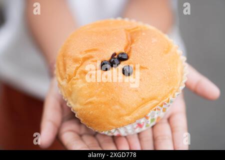 A person holding a freshly baked bun with chocolate chips on top, presented in a paper cup. Stock Photo