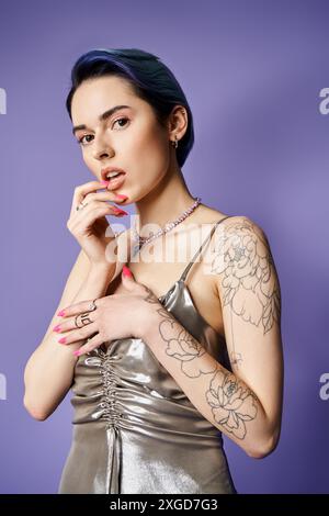 A young woman with short blue hair exhibits her tattoos in a shimmering silver dress. Stock Photo