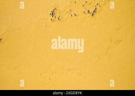 Yellow peeling paint on the old rough concrete wall,weathered rough painted wall with patterns of cracks and peeling Stock Photo