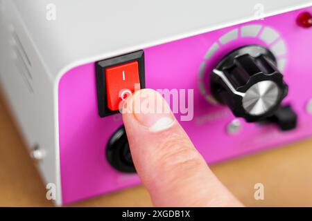 Pressing the red start switch of an electrical device with pink control panel and chrome adjustment knob with finger. Turning off the power supply Stock Photo