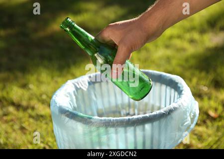 Man throwing glass bottle into garbage bin outdoors, closeup Stock Photo