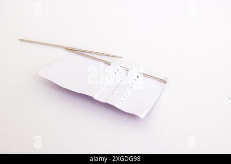 A pair of sewing needles resting on a white rectangular piece of paper, surrounded by various cosmetics and fashion accessories such as mascara and pl Stock Photo