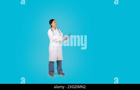 Asian Woman Doctor Using Tablet Against Blue Background Stock Photo