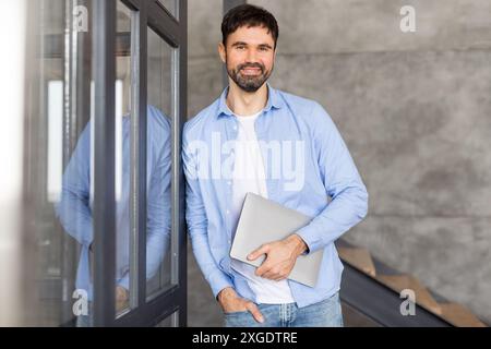Smiling Man Holding Laptop While Standing in an Office Stock Photo