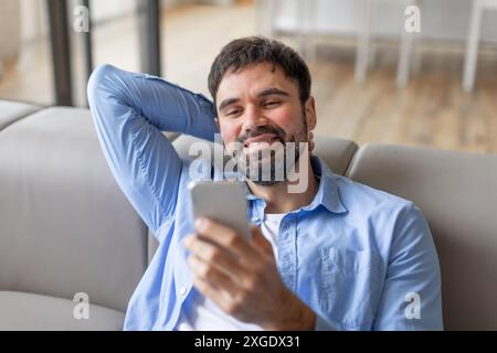 Smiling Man Using Smartphone While Relaxing on Couch Stock Photo