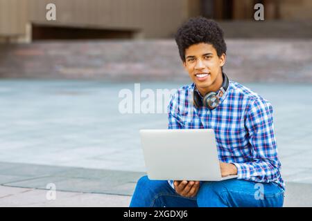 Teen Guy Smiling While Using Laptop Outdoors Stock Photo