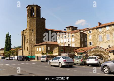 Langeac, France - May 27, 2023: A serene street with a historic church and traditional stone buildings. Cars drive by, blending contemporary life with Stock Photo