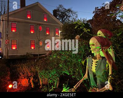 A skeleton in pirates clothes sits illuminated in the front yard while the neighbor house is lit with spooky red lights in the windows Stock Photo