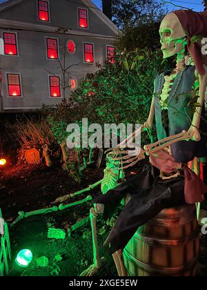 A skeleton in pirates clothes sits illuminated in the front yard while the neighbor house is lit with spooky red lights in the windows Stock Photo