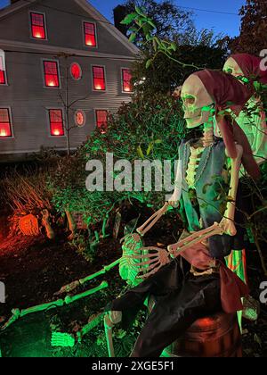 A skeleton in pirates clothes sits illuminated in the front yard while the neighbor house is lit with spooky red lights in the windows Stock Photo