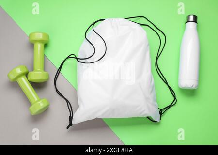 White drawstring bag, thermo bottle and dumbbells on color background, flat lay Stock Photo