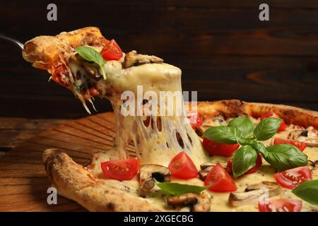 Taking piece of tasty pizza with melted cheese at wooden table, closeup Stock Photo