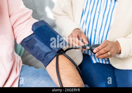 Measuring blood pressure, healthcare worker checking senior patient's arm at home Stock Photo