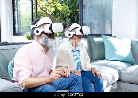 Using VR headsets, senior couple exploring virtual reality while sitting on couch Stock Photo
