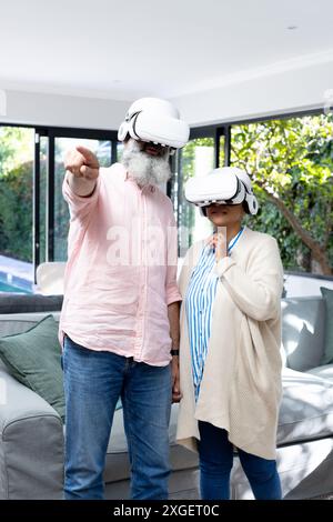 Using VR headsets, senior couple exploring virtual reality in living room Stock Photo