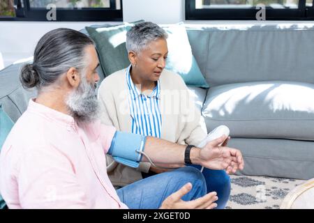Checking blood pressure, senior couple sitting on couch in living room Stock Photo
