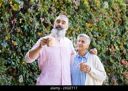 Enjoying coffee together, senior couple standing outdoors and smiling Stock Photo