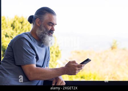 Senior man using smartphone while leaning on balcony railing, enjoying outdoors, copy space Stock Photo