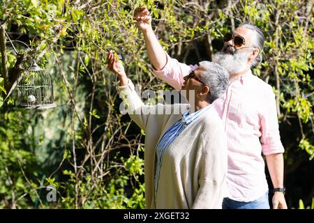 Senior couple enjoying nature, picking leaves and looking at birdcage outdoors Stock Photo
