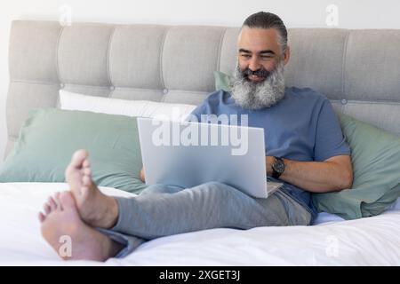 Working from home, senior man using laptop while sitting on bed Stock Photo