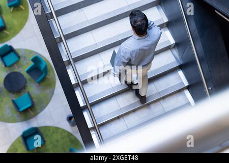 Walking down stairs, man holding laptop in modern office environment Stock Photo