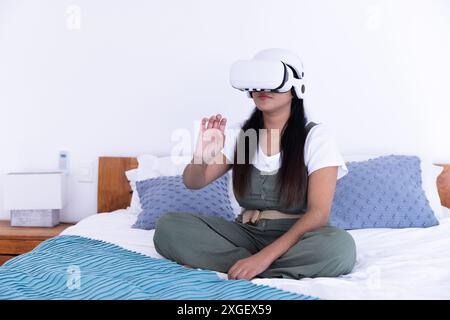 Using VR vr vr headset, woman sitting on bed and interacting with virtual environment Stock Photo