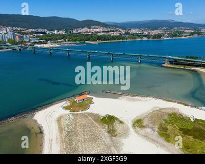 View of a city with hills connected by a bridge over a river that flows into the ocean, with a light-coloured sandy beach and clear water, aerial Stock Photo