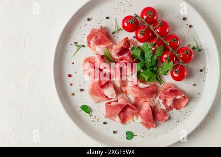 Sliced prosciutto, appetizer, with cherry tomatoes, on a white plate, top view Stock Photo