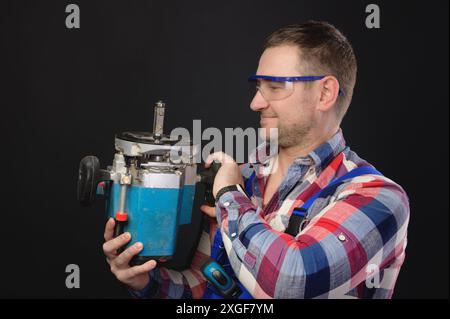 Friendly caucasian male carpenter with a wood cutter in his hands. Portrait of a man working with a tree on a black background Stock Photo
