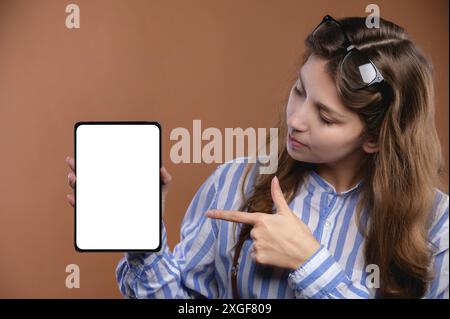 Young happy caucasian woman in shirt and glasses holds index finger on laptop computer with blank screen workspace, studio portrait Stock Photo