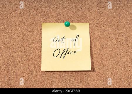 Yellow note with phrase out of office on cork board Stock Photo