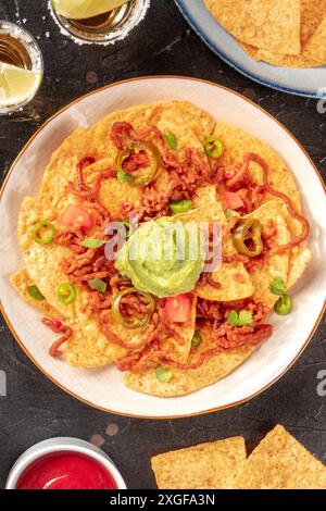 A plate of nachos, Mexican tortilla chips, overhead shot on a black background Stock Photo