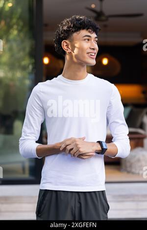 Wearing smartwatch, smiling young man standing outside modern home Stock Photo