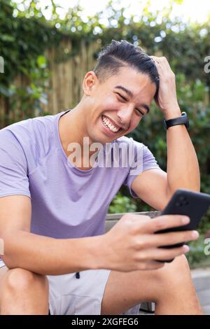 Smiling man using smartphone and sitting outdoors, enjoying leisure time Stock Photo