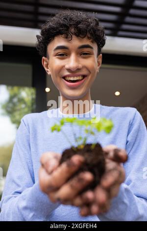 Smiling young man holding small plant with soil, enjoying gardening at home Stock Photo