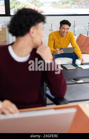 Laughing and holding smartphone, man sitting on couch while other man working Stock Photo