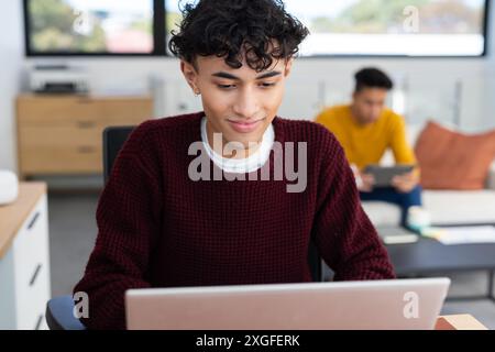 Using laptop, young man working while partner uses tablet in background Stock Photo