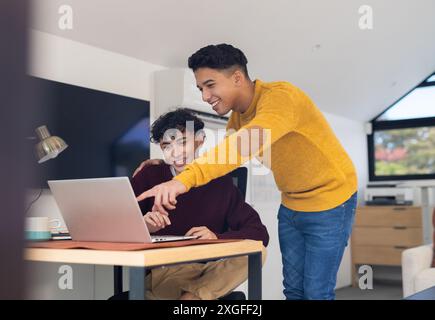 Smiling gay couple using laptop together, pointing at screen in home office Stock Photo