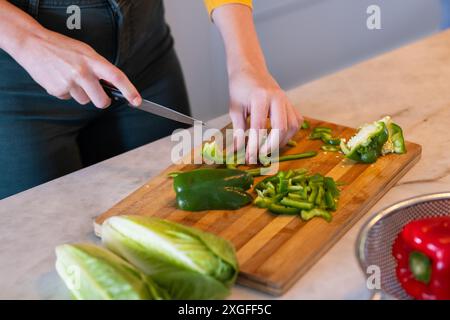 Chopping green bell peppers on cutting board, person preparing fresh vegetables Stock Photo