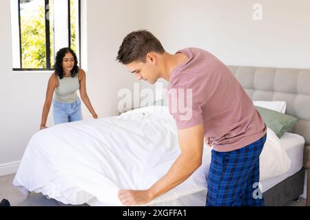 Making bed together, young couple tidying bedroom in morning routine Stock Photo