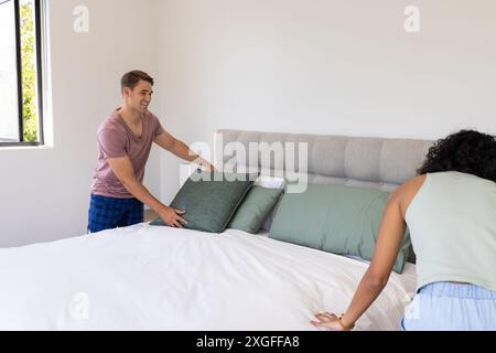 Young couple making bed together, arranging pillows in bright bedroom, copy space Stock Photo
