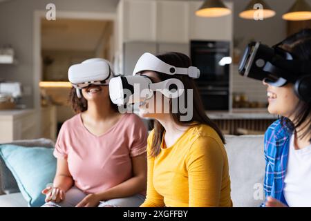 Using VR headsets, three women friends enjoying virtual reality experience at home Stock Photo