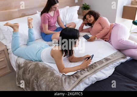 Relaxing on bed, three women friends using smartphones and tablet at home Stock Photo