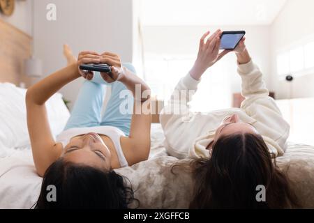 Using smartphones, two women friends lying on bed and browsing in bedroom Stock Photo