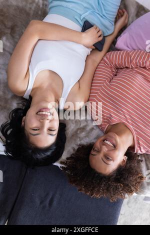 Lying on bed, two women friends smiling and relaxing with smartphone in hand Stock Photo